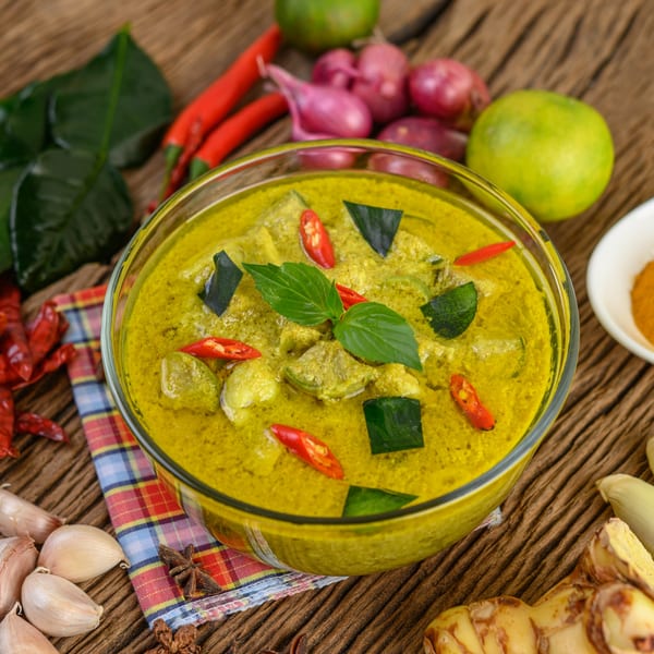 Spoon Thai Kitchen's green curry with basil, chilies, and vegetables, surrounded by fresh ingredients.