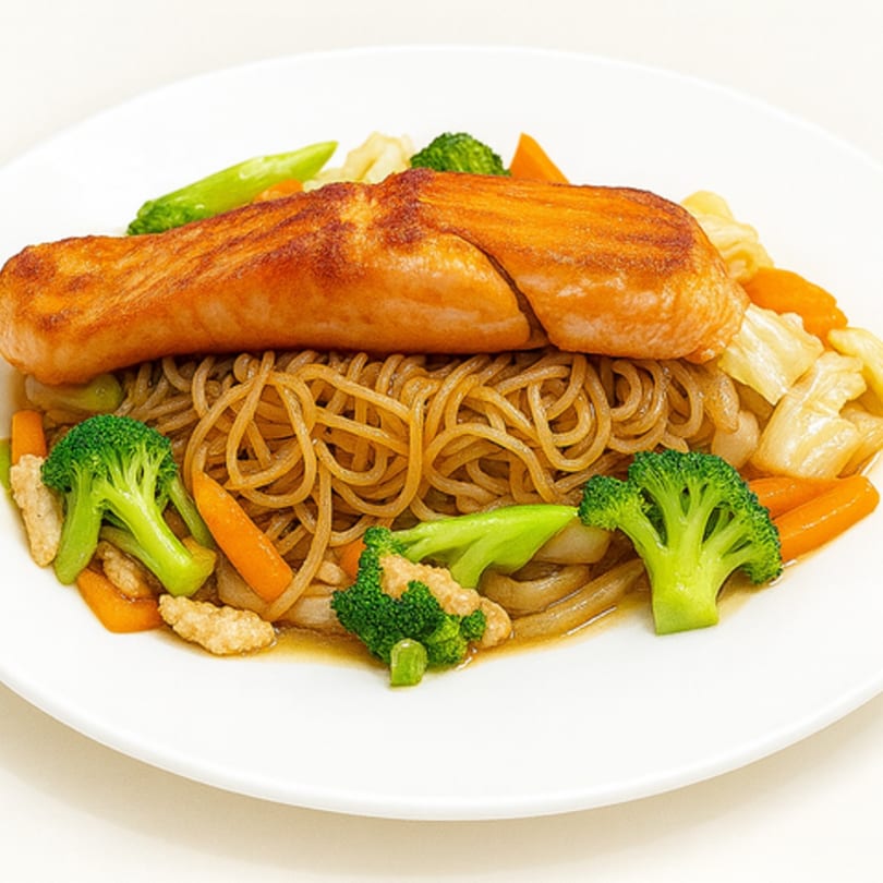 Grilled salmon fillet over noodles with broccoli, carrots, and cabbage on a white plate.